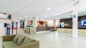 Un vestíbulo amplio con mostrador de recepción, una escalera, máquina expendedora y un sofá.