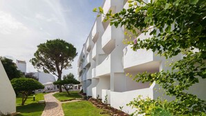 Un edificio moderno con paredes exteriores blancas y un camino de piedra que conduce a una entrada bordeada de árboles.