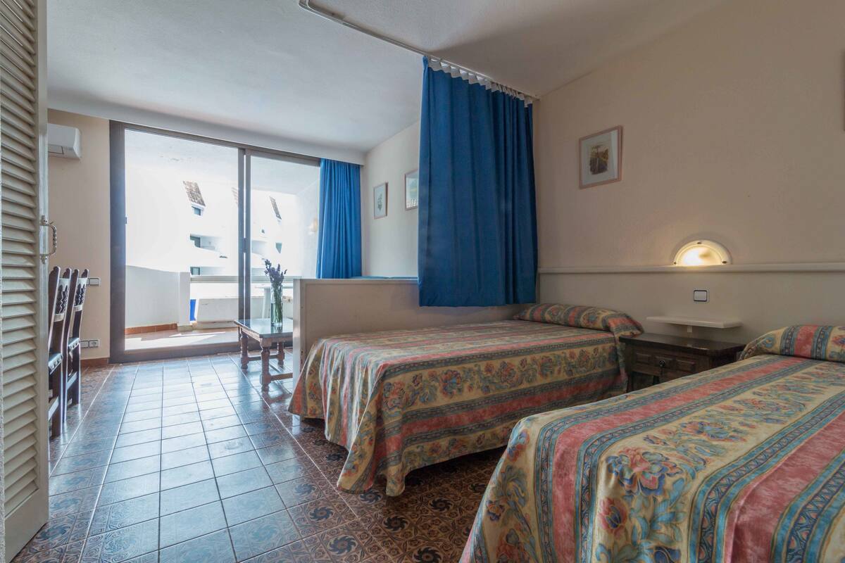 A hotel room with two beds, a balcony, and a view of a building outside.
