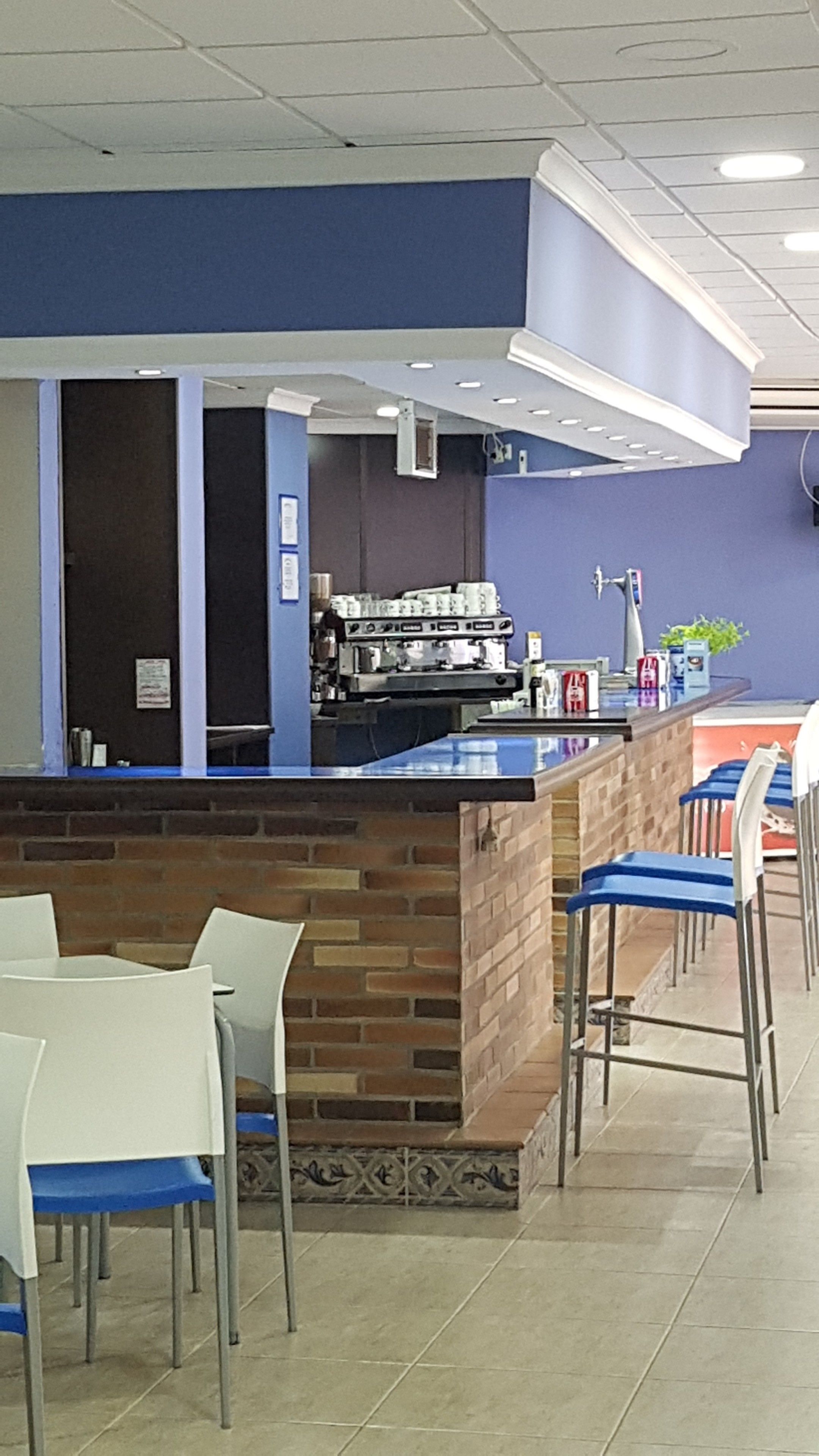 A cafe with a blue counter, brick wall, and white chairs.