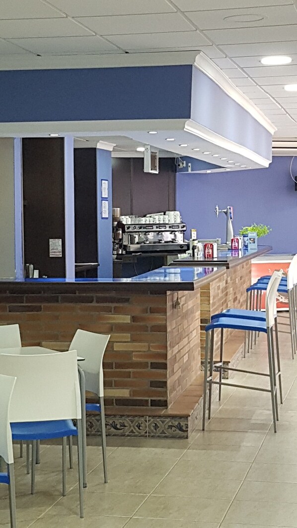 Un café con mostrador azul, pared de ladrillo y sillas blancas.