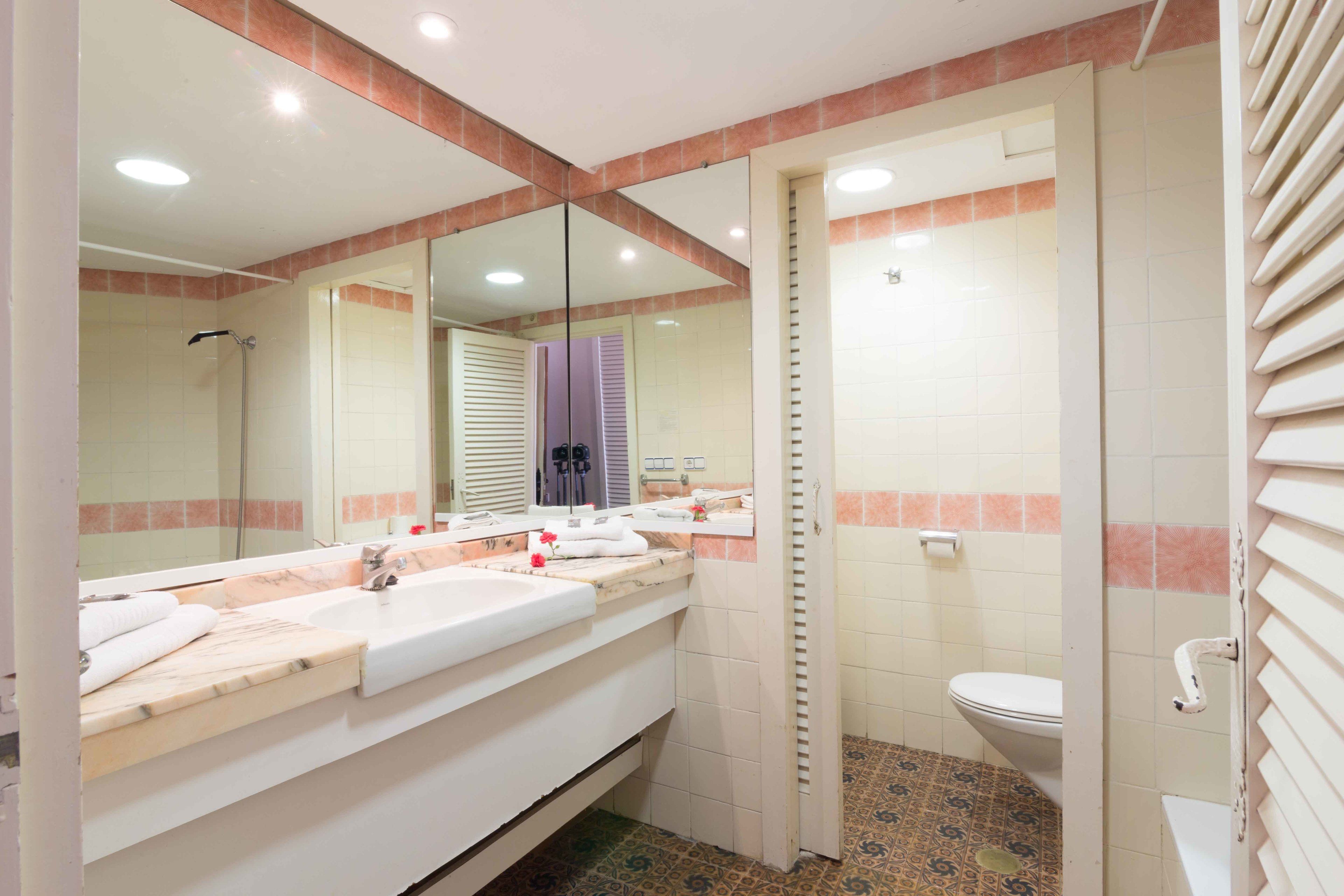 A bathroom with a large mirror, a sink, a toilet, and a shower.