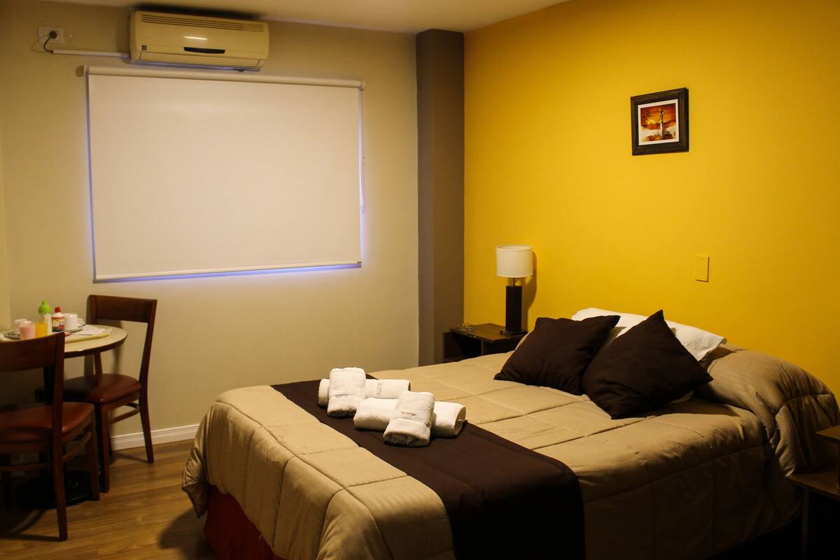 A hotel room with a bed, a desk, a chair, a lamp, and a picture on the wall.