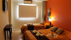Habitación de hotel con dos camas, una mesita de noche, televisión, aire acondicionado, ventana con persianas, un cuadro en la pared y una bandeja con productos para el desayuno.