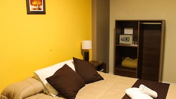 A hotel room with a bed, pillows, a bedside table with a lamp, a radio, and a wardrobe.