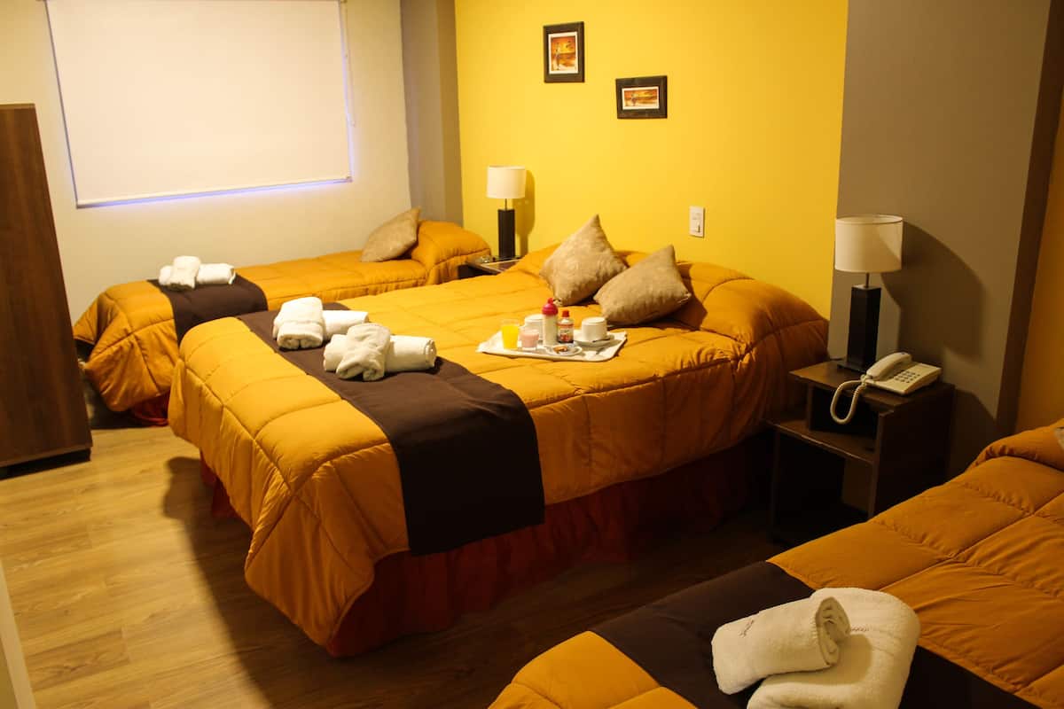 A hotel room with two beds, each with a yellow bedspread and pillows, a bedside table with a lamp, a phone, and a tray with breakfast items.