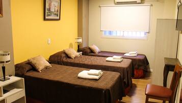 A hotel room with two beds, a desk, a chair, an air conditioner, and a window with blinds.