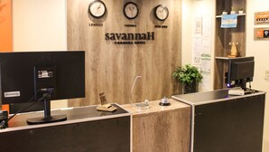Una recepción de hotel con relojes mostrando diferentes zonas horarias, un monitor de computadora y una pared de madera con el nombre del hotel.