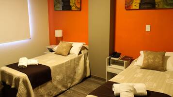 Une chambre d’hôtel avec deux lits, chacun recouvert d’une couverture marron et agrémenté d’oreillers blancs. On y trouve une table de chevet avec une lampe et un téléphone. Les murs sont de couleur orange et ornés de peintures abstraites.
