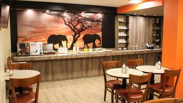 Un restaurante con mostrador de comida, sillas de madera y un mural de un elefante en la pared.