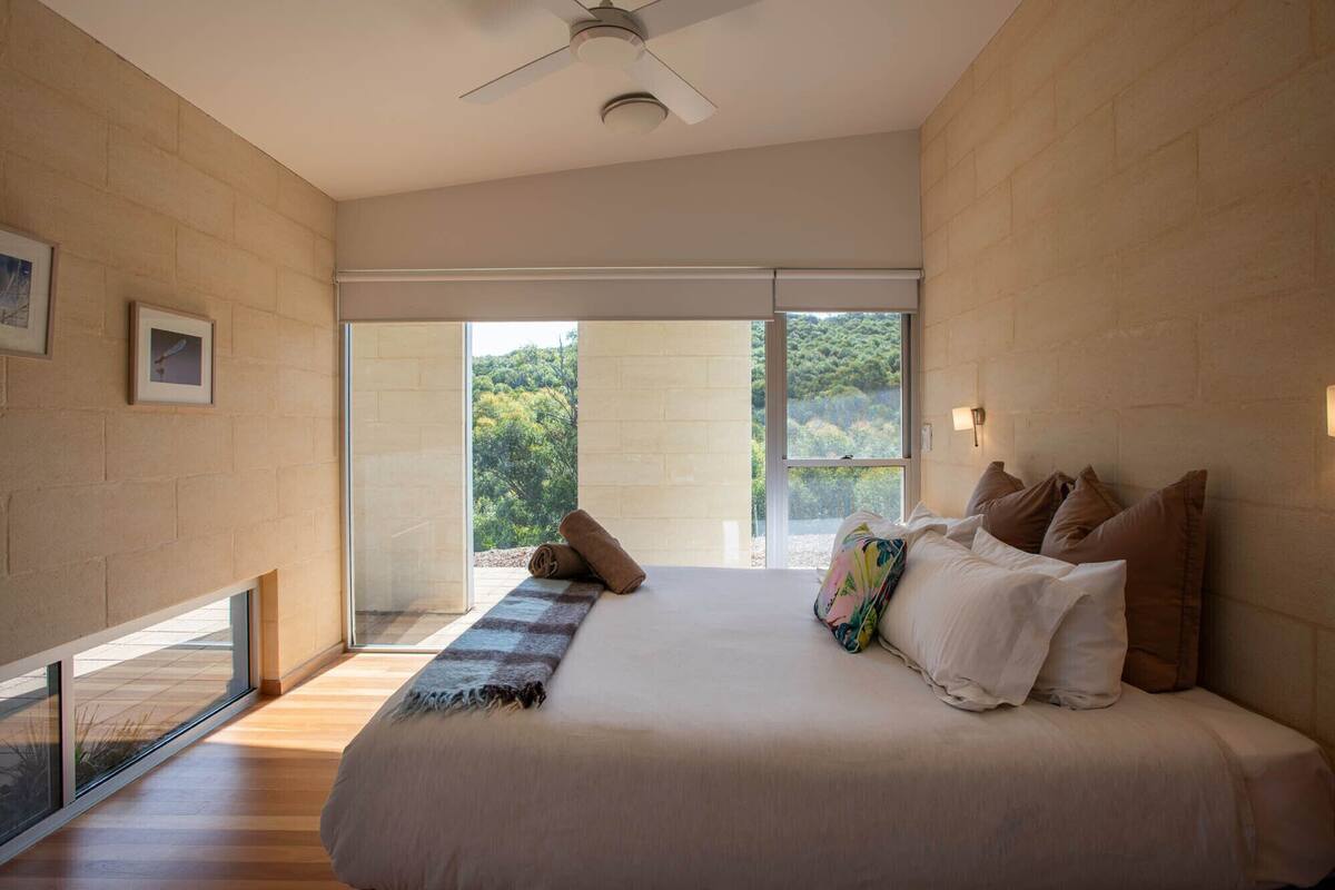 Un dormitorio moderno con una cama grande, vistas al verdor por la ventana y un ventilador de techo.