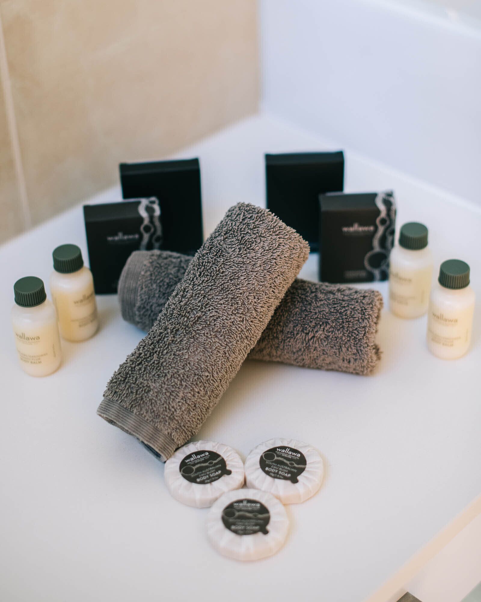 Un baño con un lavamanos blanco, dos toallas y varias botellas de jabón de baño.