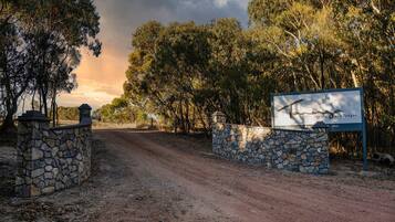 A dirt road leading to a stone wall entrance with a sign for luxury eco lodges.