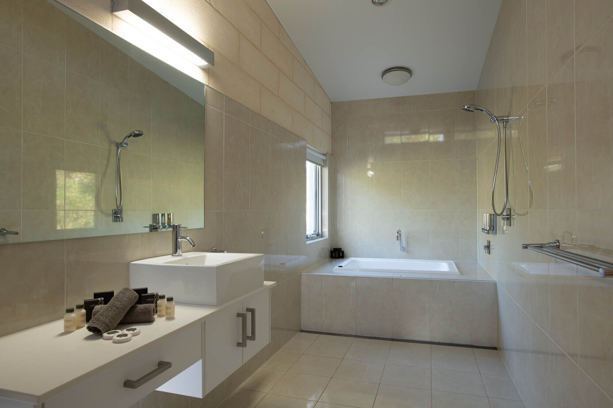 A modern bathroom with a large mirror, two sinks, a bathtub, and a shower.