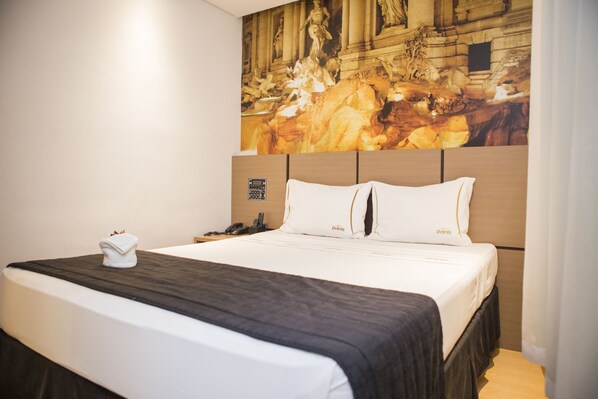 A hotel room with a large bed, a headboard with a classical painting, a telephone, and a folded towel on the bed. - Palais Hotel (Sao Vicente)