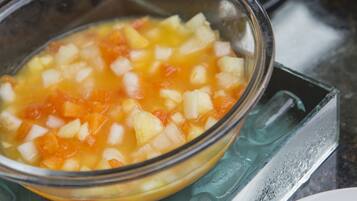 Un tazón de vidrio con fruta cortada en cubos y una mezcla líquida sobre una encimera de cocina.