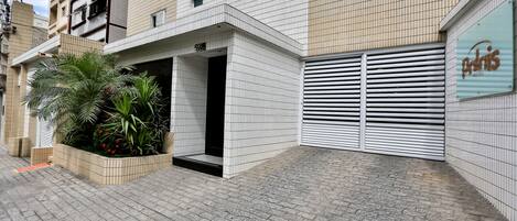 A hotel entrance with a tiled facade, a planter with greenery, and a closed garage door.