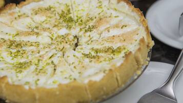 Una tarta redonda con corteza, cubierta con un relleno cremoso blanco y hierbas verdes, servida en un plato blanco con una cuchara metálica.