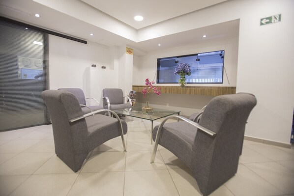 Un área de espera con una mesa de vidrio, dos sillones grises y un jarrón con flores rosadas.