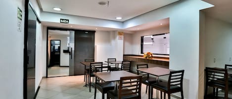 A dining area with tables and chairs, a sign indicating the exit, and a bulletin board on the wall.