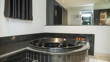 Un baño moderno con una bañera grande, encimeras de mármol negro y un espejo que refleja un mueble de tocador y un adorno de pared.