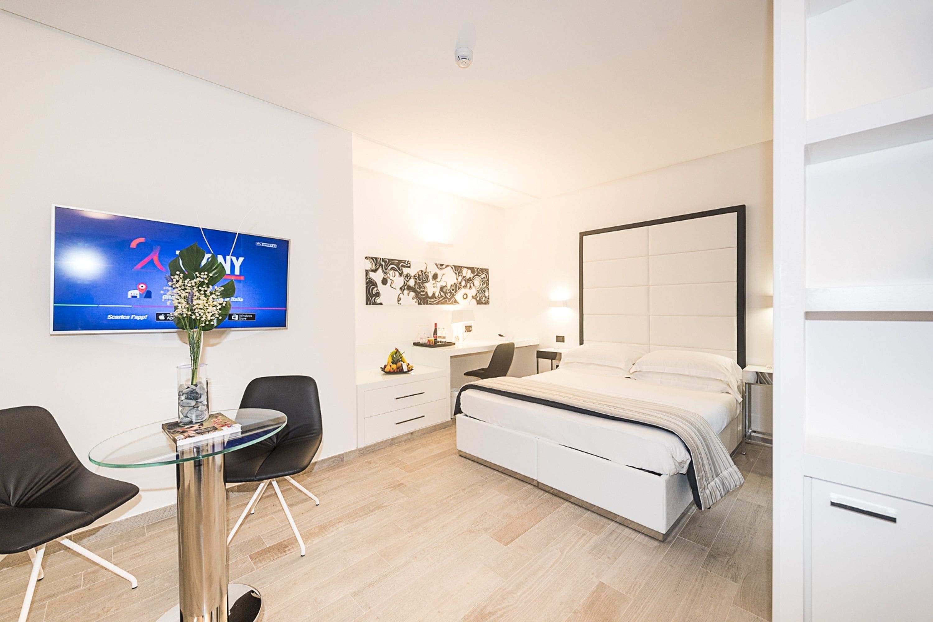 Una habitación de hotel moderna con cama, escritorio, sillas y televisión en la pared.