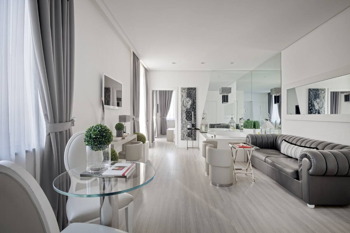 A modern living room with a glass coffee table, grey sofa, and a dining area with a glass table.