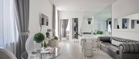 A modern living room with a glass coffee table, grey sofa, and a dining area with a glass table.