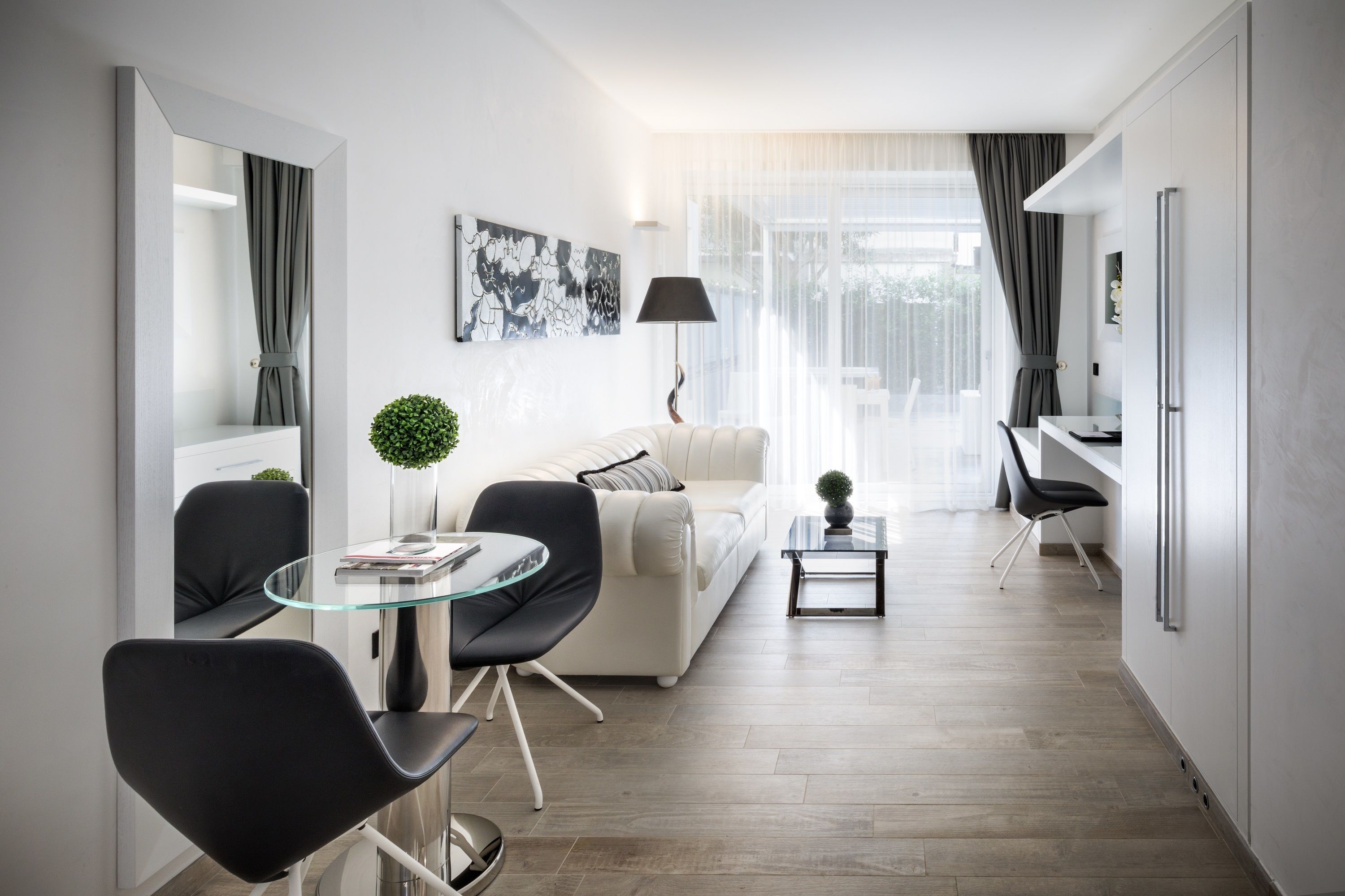 A modern living room with a glass dining table, black chairs, a white sofa, and a small side table with a plant.