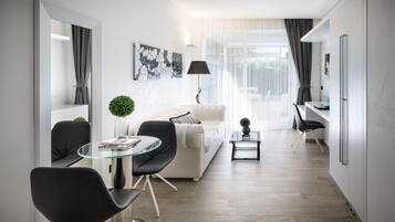 A modern living room with a glass dining table, black chairs, a white sofa, and a small side table with a plant.
