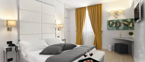 A modern hotel room with a large bed, bedside lamps, a small table with a tray of fruit and wine, and a painting on the wall.