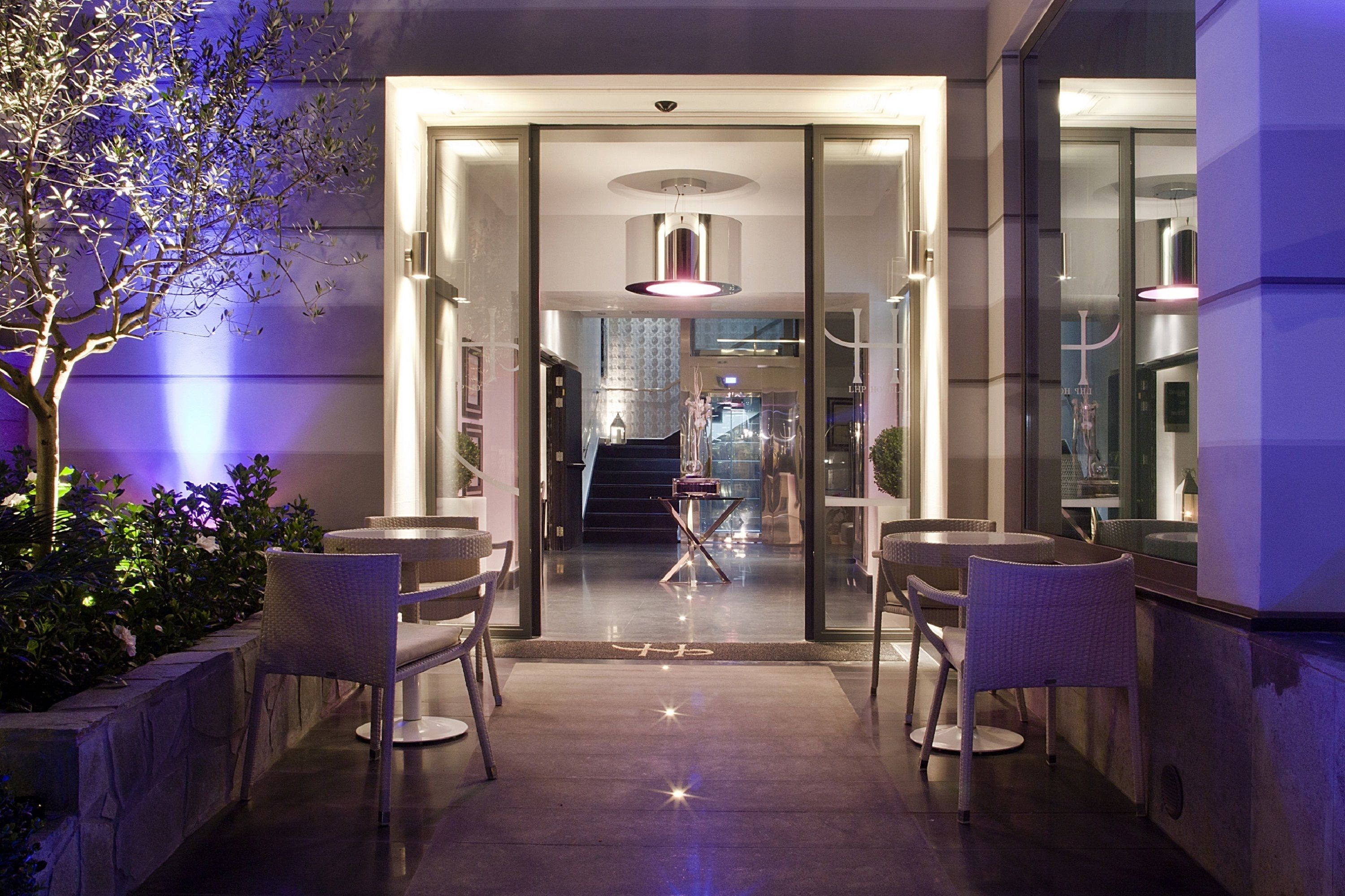 An entrance with glass doors leading to a lobby, featuring a staircase and a table with chairs.