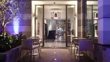 An entrance with glass doors leading to a lobby, featuring a staircase and a table with chairs.