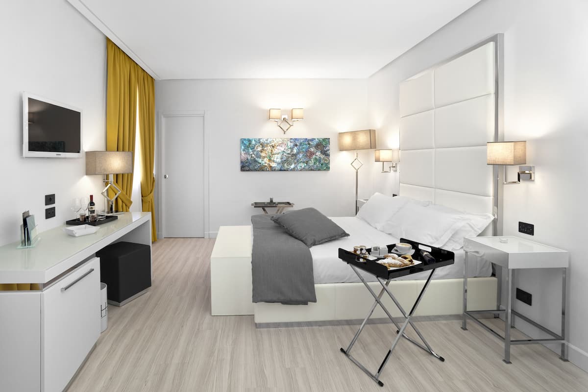 A modern hotel room with a bed, bedside tables, a desk, and a painting on the wall.