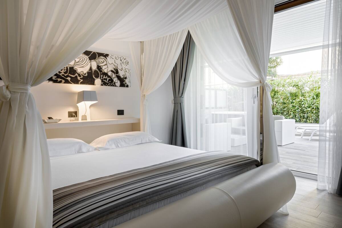 A modern bedroom with a large bed, a bedside table with a lamp, and a view of an outdoor patio.