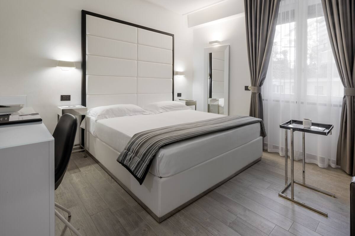 A modern hotel room with a large bed, bedside tables, a desk, and a chair.