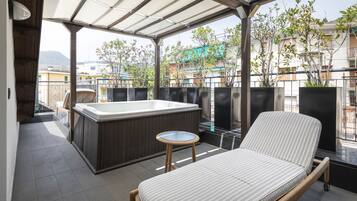 A balcony with a hot tub, a cushioned chair, and potted plants.