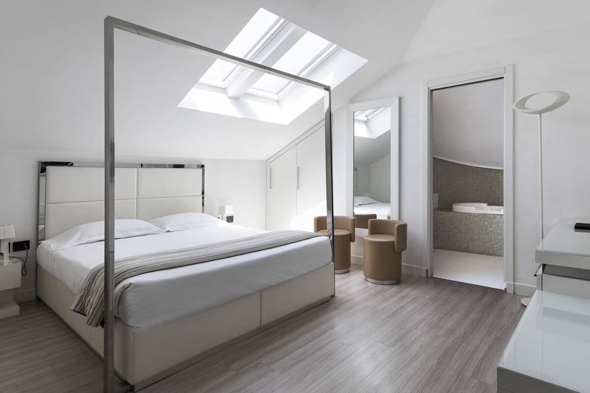A modern bedroom with a skylight, a large bed, a walk-in closet, and a bathroom with a curved sink.