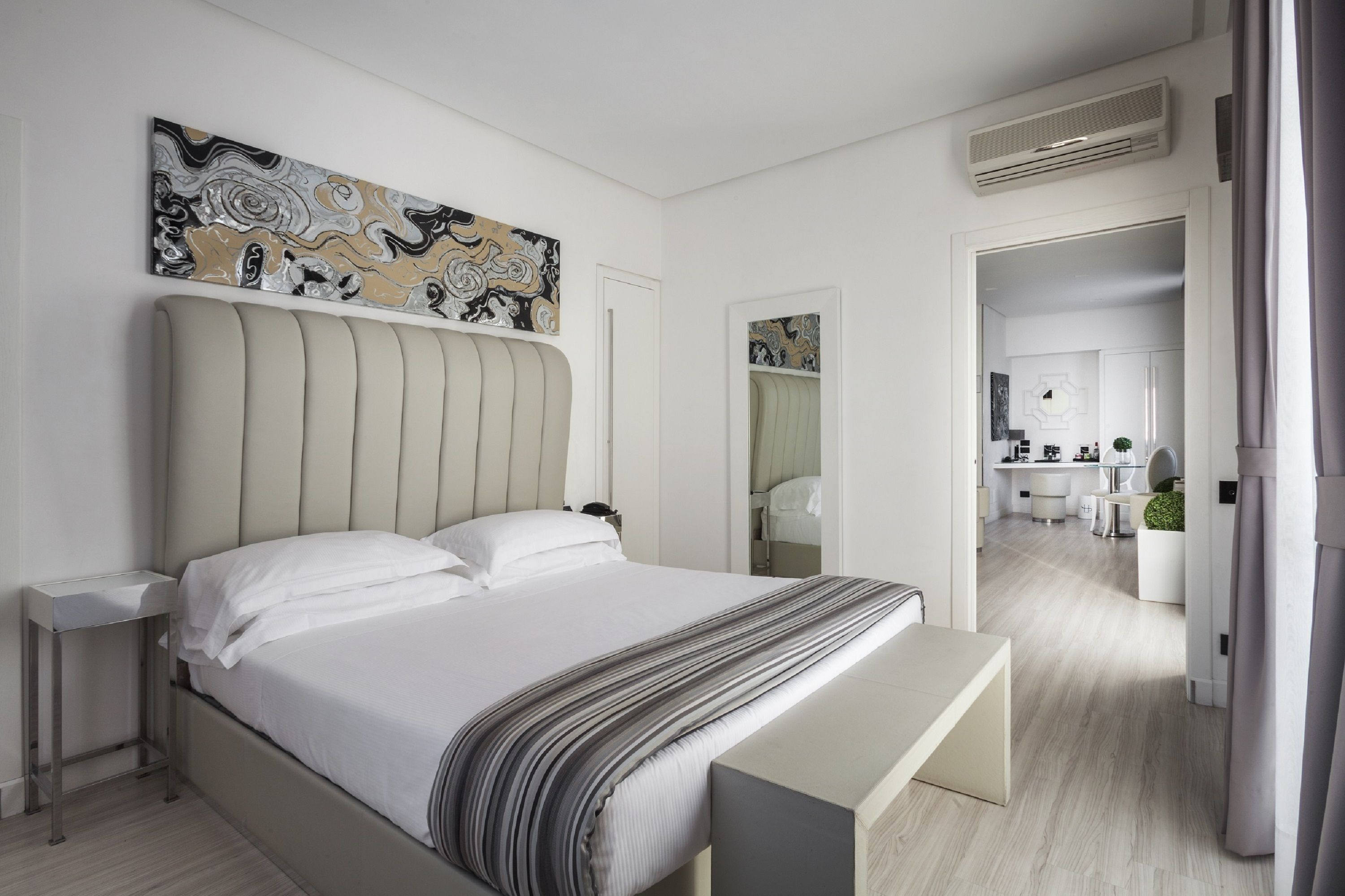 A modern bedroom with a large bed, bedside tables, a bench, and a painting on the wall.