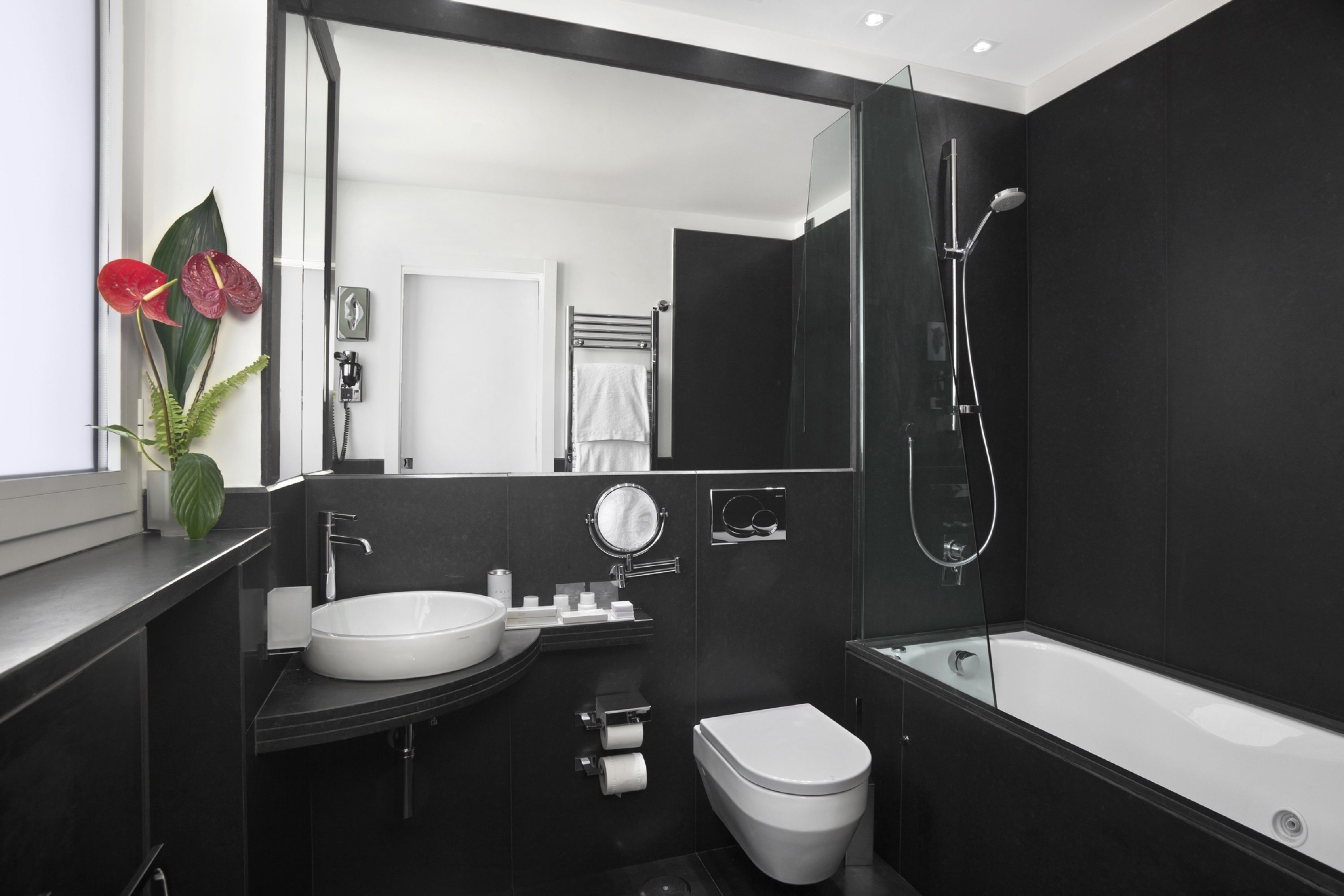 Ein modernes Badezimmer mit Waschbecken, Toilette und Badewanne in Weiß. Es verfügt über einen großen Spiegel, einen Handtuchhalter und eine Dusche.