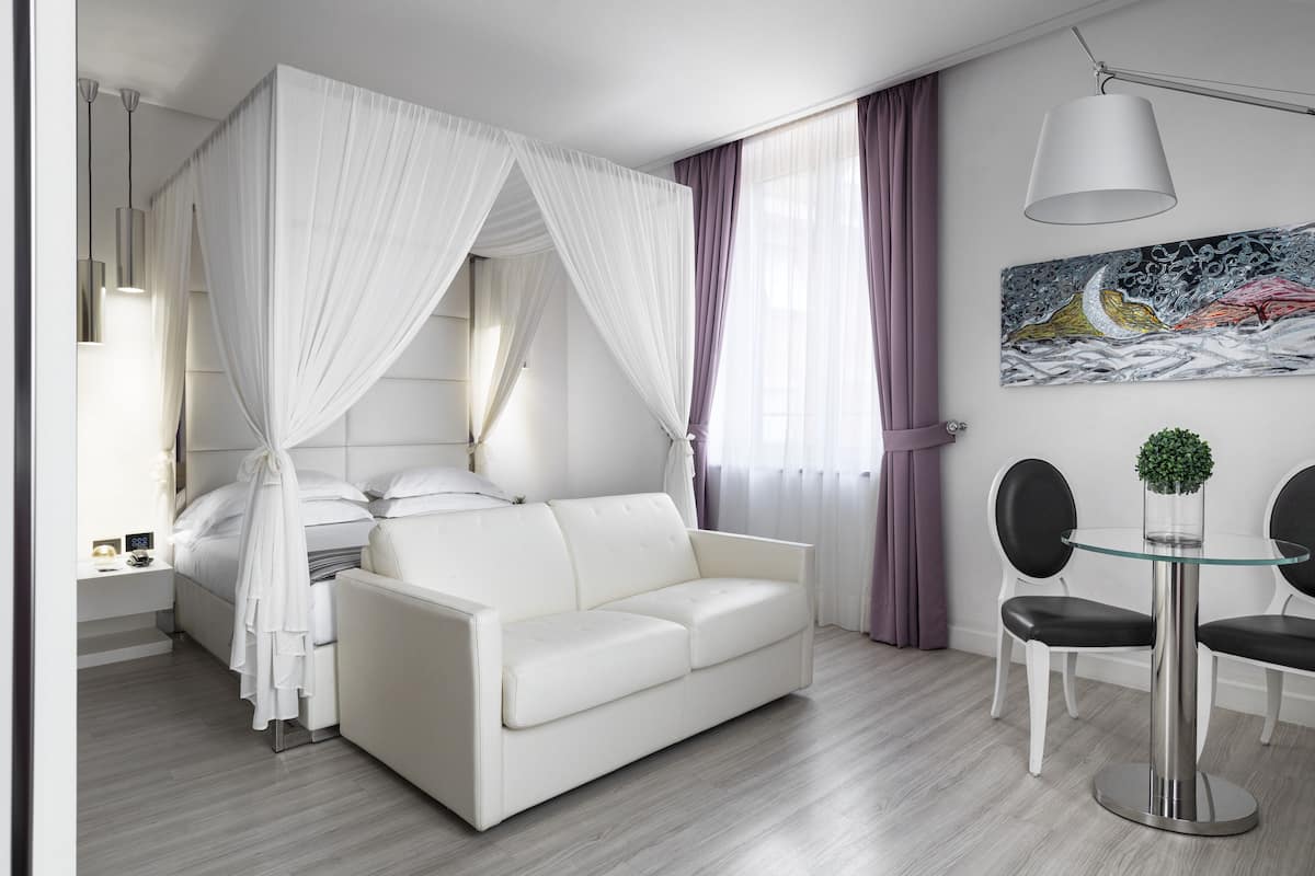 A modern hotel room with a white sofa, a glass table, and a painting on the wall.