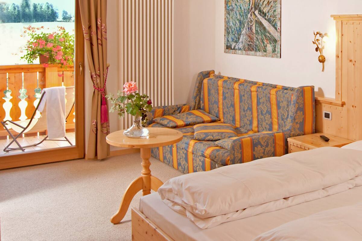 A bedroom with a large bed, a sofa, a small table with a vase of flowers, and a wooden headboard.