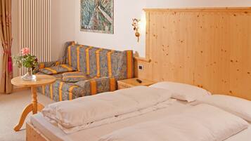 A bedroom with a large bed, a sofa, a small table with a vase of flowers, and a wooden headboard.