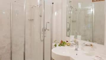 Un baño moderno con ducha de vidrio, un lavabo blanco con espejo y vigas de madera en el techo.