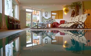 A modern indoor pool area with lounge chairs and a glass wall reflecting the pool.
