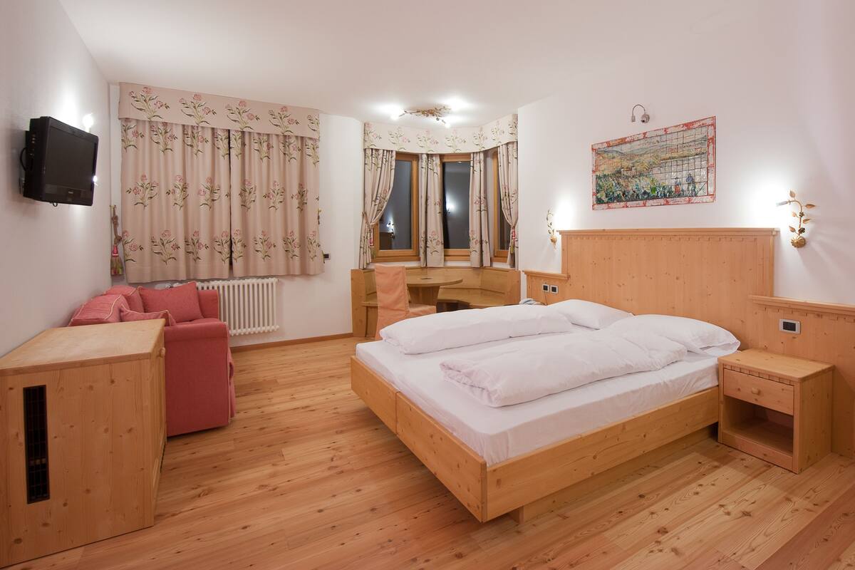 A bedroom with a wooden bed, a red sofa, a wooden nightstand, a wooden dresser, and a wall-mounted TV.