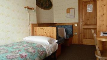 A small bedroom with a single bed, a wooden door, and a small table.