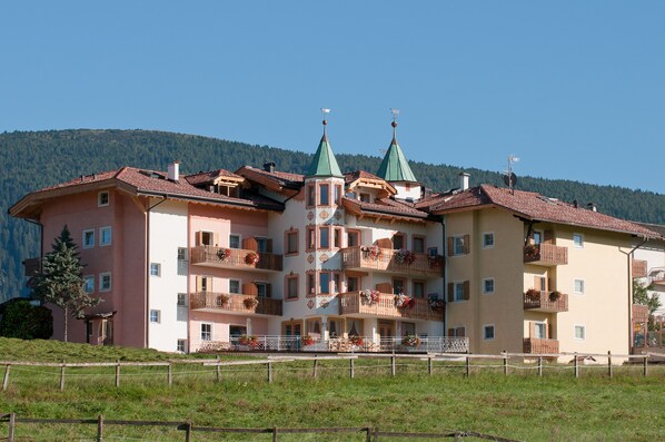 A multi-story hotel with balconies, a central entrance, and a mountainous backdrop.