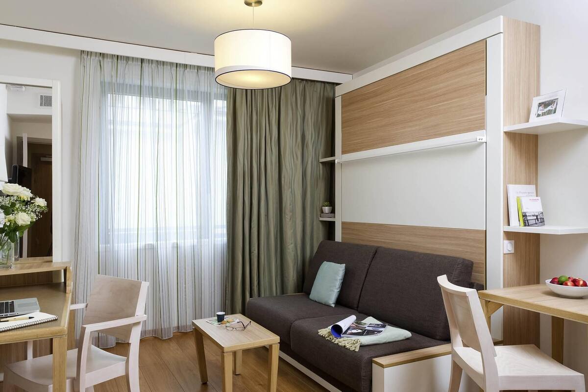 Un salon moderne comprenant un canapé, deux fauteuils, une petite table, une lampe, une bibliothèque et une fenêtre avec des rideaux.