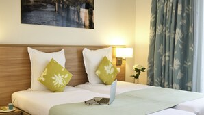 A hotel room with a bed, a nightstand, a lamp, a painting, and a window with curtains.